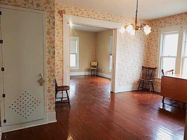 interior space with dark wood-style flooring, a notable chandelier, baseboards, and wallpapered walls