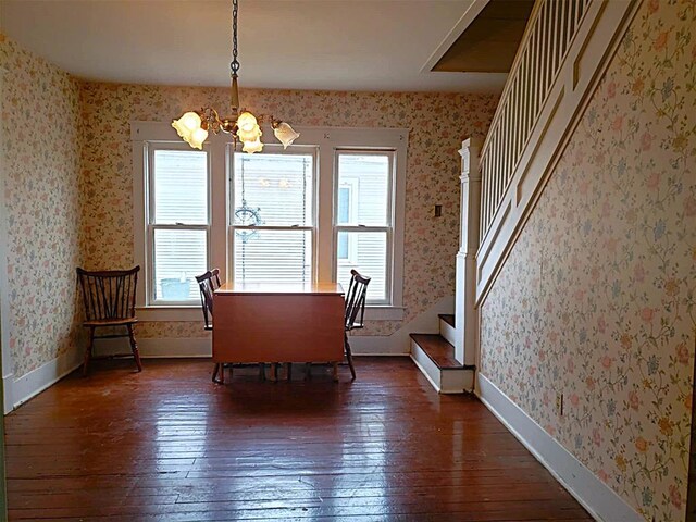 unfurnished dining area with dark wood-style flooring, baseboards, stairway, wallpapered walls, and an inviting chandelier