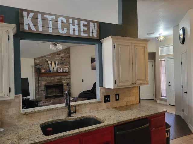 kitchen with light stone counters, tasteful backsplash, a large fireplace, a sink, and dishwasher