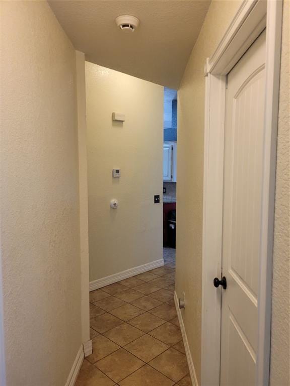 corridor with a textured wall, baseboards, and light tile patterned floors