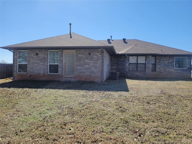 rear view of house with central AC, brick siding, a lawn, and a shingled roof