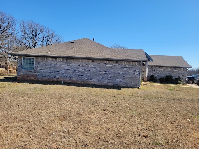 view of property exterior featuring roof with shingles, a lawn, and brick siding