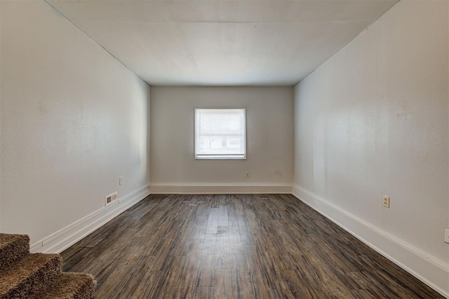 unfurnished room featuring dark wood-style floors, baseboards, stairway, and visible vents