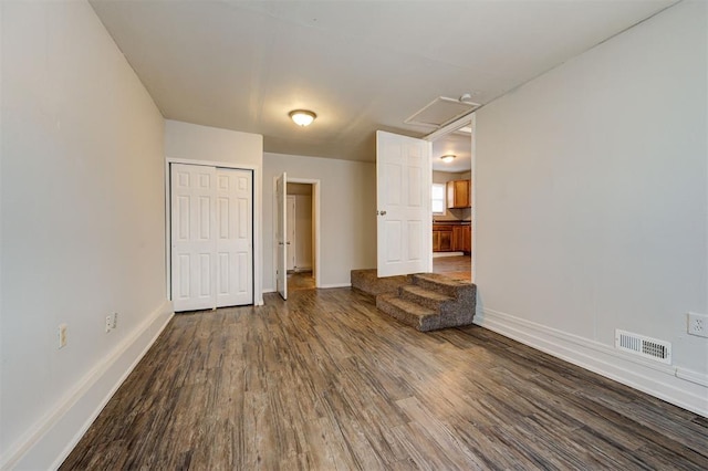 unfurnished room with attic access, wood finished floors, visible vents, and baseboards