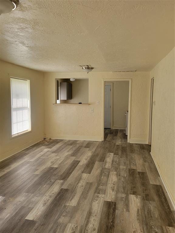 unfurnished room featuring baseboards, dark wood finished floors, a textured ceiling, and a textured wall