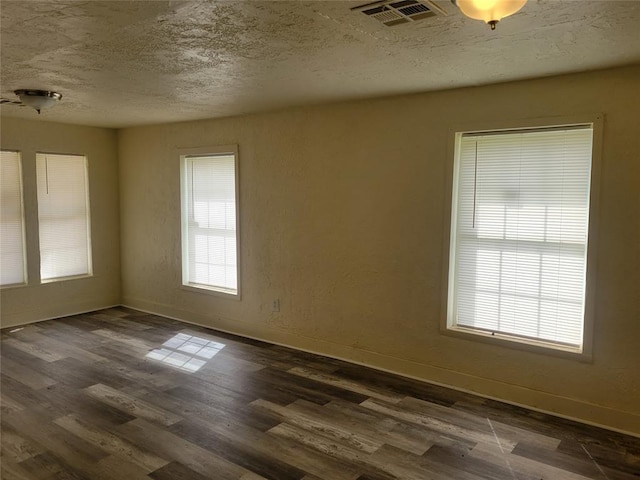 empty room featuring dark wood-type flooring, visible vents, a textured ceiling, and baseboards