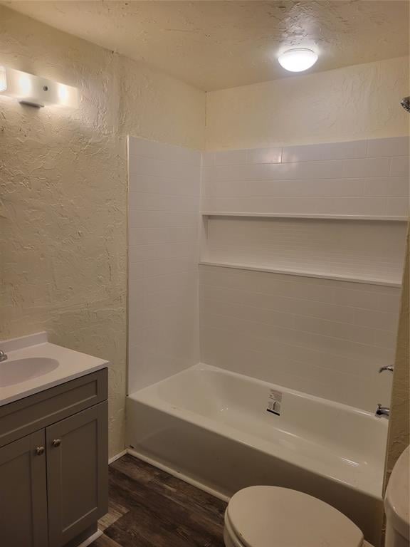 bathroom with shower / bathing tub combination, a textured wall, toilet, vanity, and wood finished floors