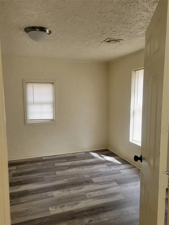 spare room featuring a textured ceiling, a textured wall, dark wood finished floors, and visible vents