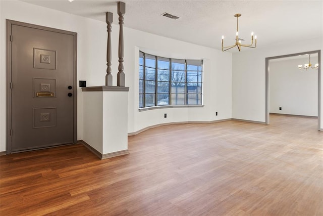 foyer entrance with an inviting chandelier, baseboards, visible vents, and wood finished floors