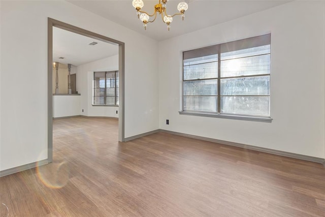 unfurnished room with baseboards, visible vents, a chandelier, and wood finished floors