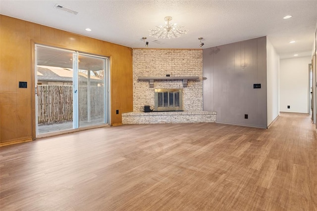 unfurnished living room with light wood finished floors, visible vents, a large fireplace, wooden walls, and a textured ceiling