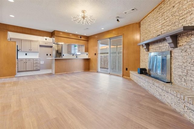 unfurnished living room with visible vents, a large fireplace, a sink, a textured ceiling, and light wood-type flooring