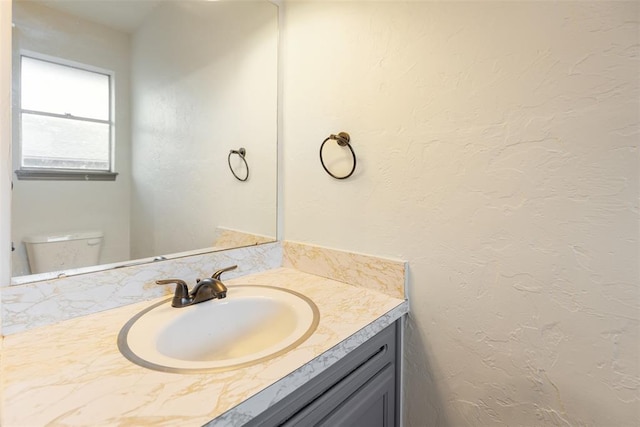 bathroom with toilet, a textured wall, and vanity