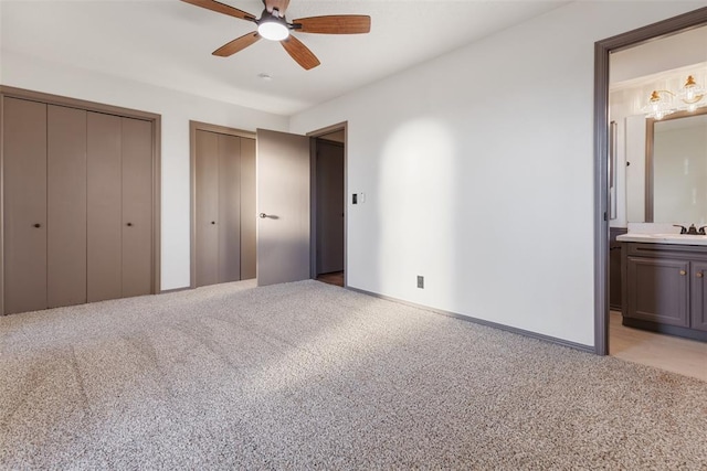 unfurnished bedroom featuring light carpet, a sink, ensuite bathroom, and two closets