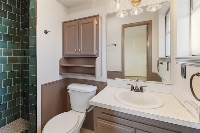 full bathroom with toilet, tiled shower, and vanity