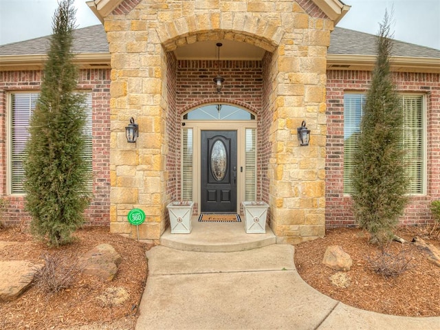 entrance to property with stone siding, roof with shingles, and brick siding