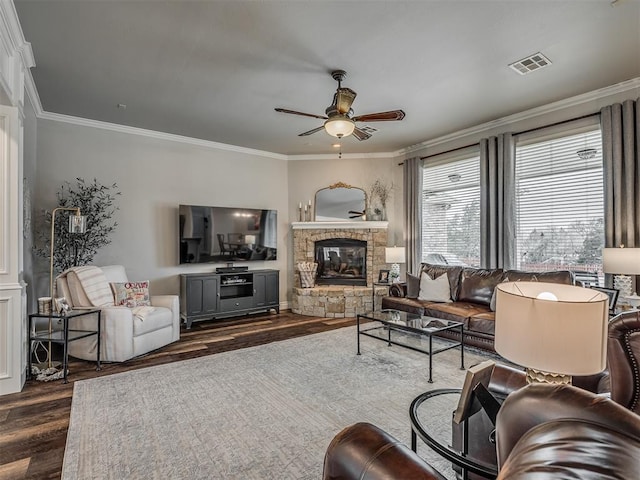 living room with visible vents, a ceiling fan, dark wood-style flooring, crown molding, and a stone fireplace