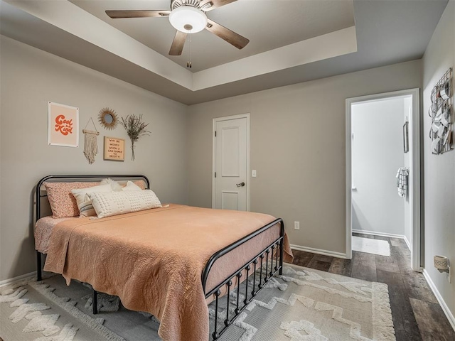 bedroom featuring wood finished floors, a raised ceiling, and baseboards