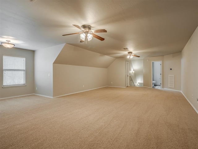 additional living space featuring light carpet, visible vents, baseboards, a ceiling fan, and vaulted ceiling