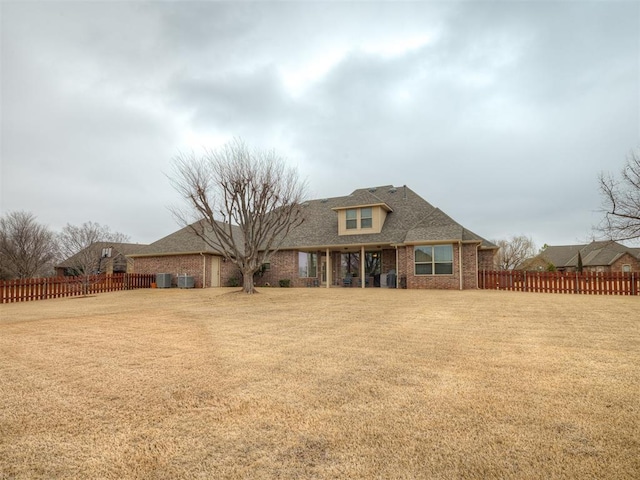 view of front facade with brick siding, a front yard, fence, and a shingled roof