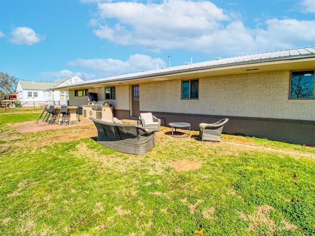 back of property featuring an outdoor kitchen, a lawn, a patio, metal roof, and brick siding