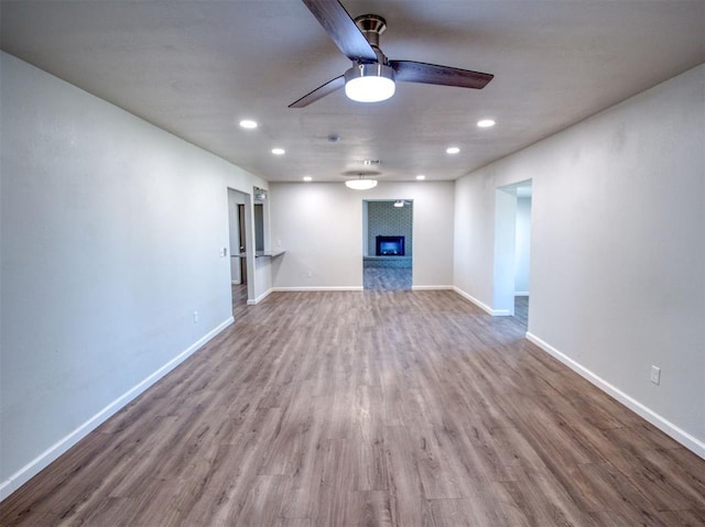 unfurnished living room with a large fireplace, ceiling fan, wood finished floors, and baseboards