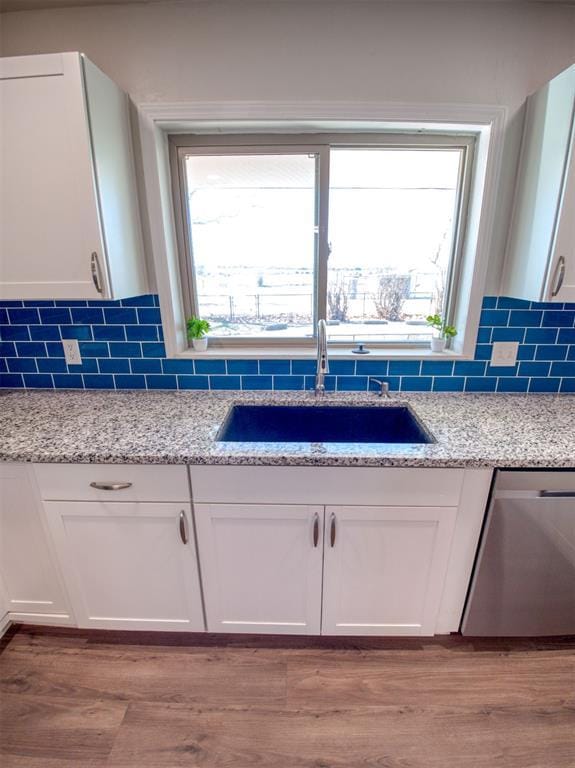 kitchen with light stone counters, a sink, white cabinetry, backsplash, and dishwasher