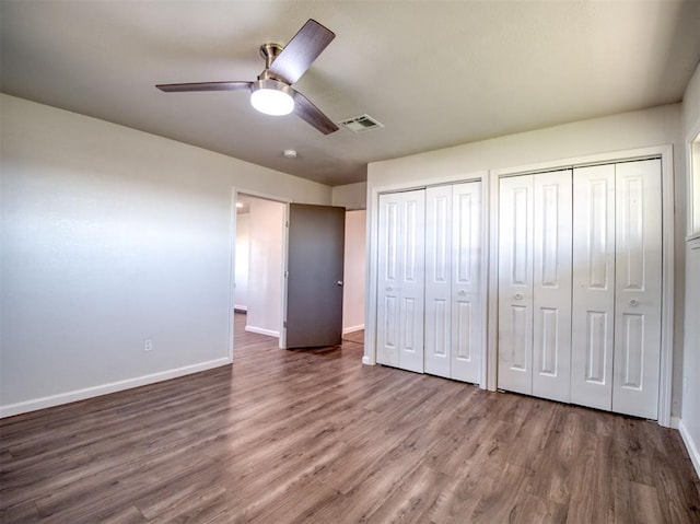 unfurnished bedroom with baseboards, visible vents, two closets, and wood finished floors