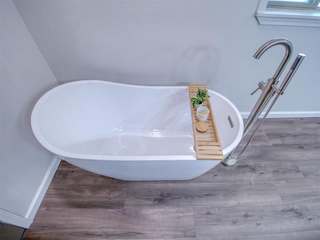 interior details featuring a freestanding bath, baseboards, and wood finished floors