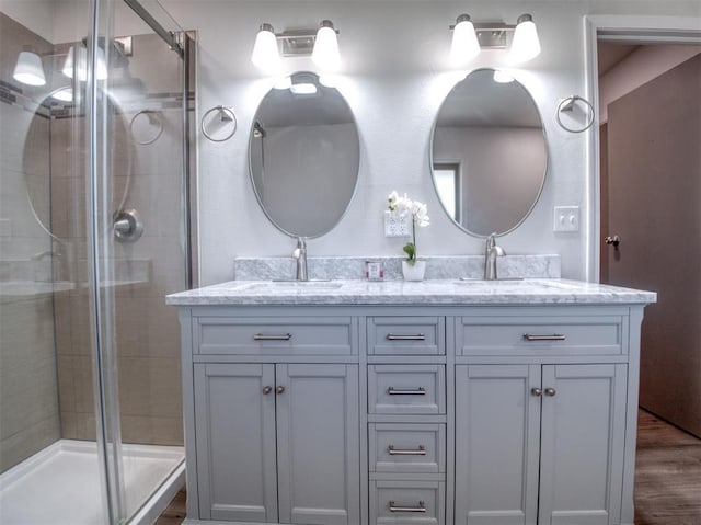 bathroom featuring double vanity, wood finished floors, a sink, and a shower stall