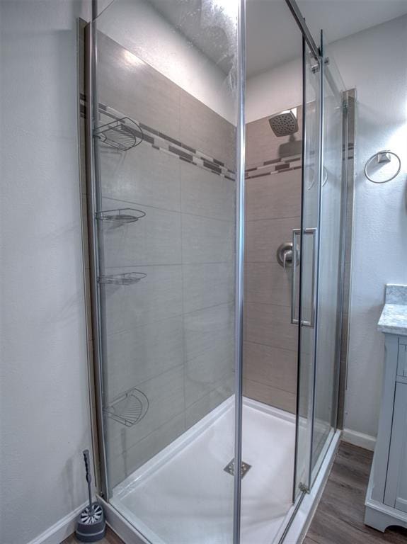 full bathroom with a stall shower, vanity, baseboards, and wood finished floors