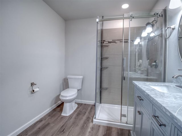 bathroom featuring toilet, a stall shower, vanity, wood finished floors, and baseboards