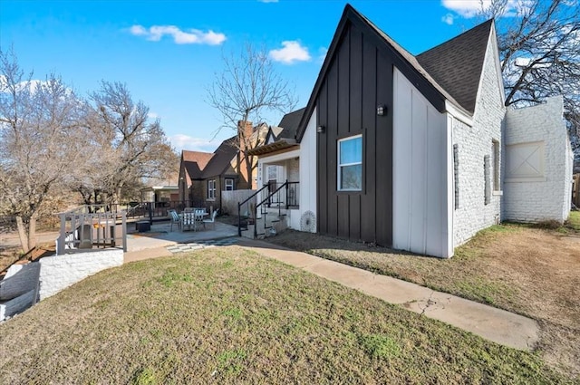 view of property exterior featuring brick siding, a shingled roof, a lawn, board and batten siding, and a patio area