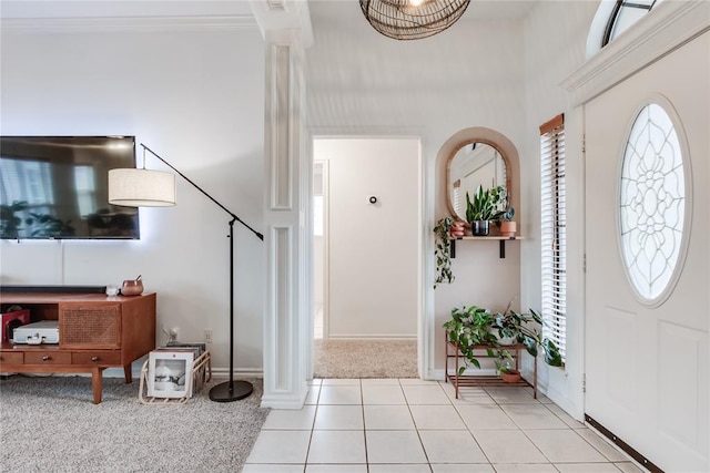 entrance foyer featuring light carpet, light tile patterned floors, decorative columns, baseboards, and crown molding