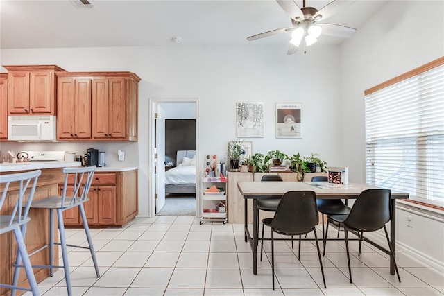 kitchen with light tile patterned floors, ceiling fan, white microwave, light countertops, and brown cabinets