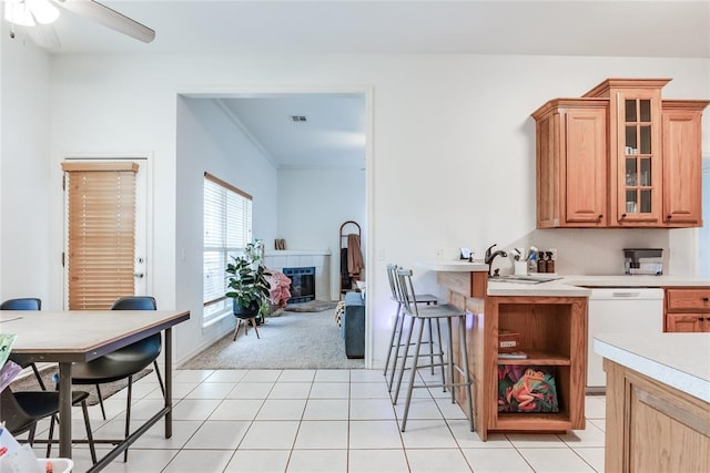 kitchen featuring light tile patterned floors, a fireplace, light countertops, dishwasher, and glass insert cabinets