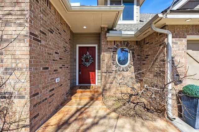 property entrance featuring brick siding and a shingled roof