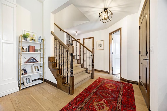 entryway featuring baseboards, a chandelier, stairs, and light wood finished floors