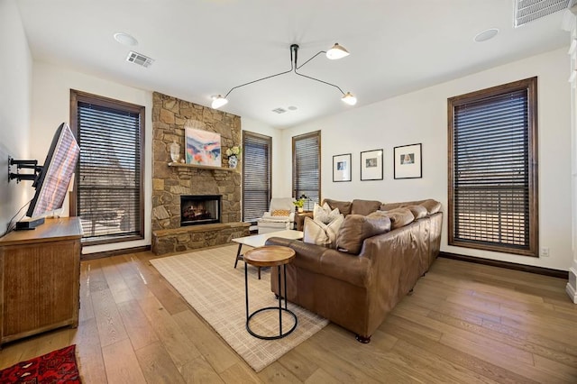 living area with visible vents, a stone fireplace, and hardwood / wood-style flooring