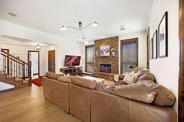 living area with visible vents, light wood-style flooring, stairs, a stone fireplace, and a chandelier