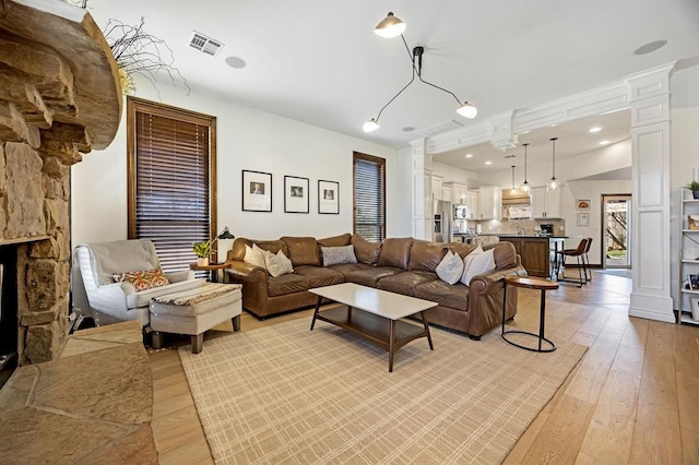 living area featuring visible vents, a stone fireplace, recessed lighting, light wood-style flooring, and ornate columns