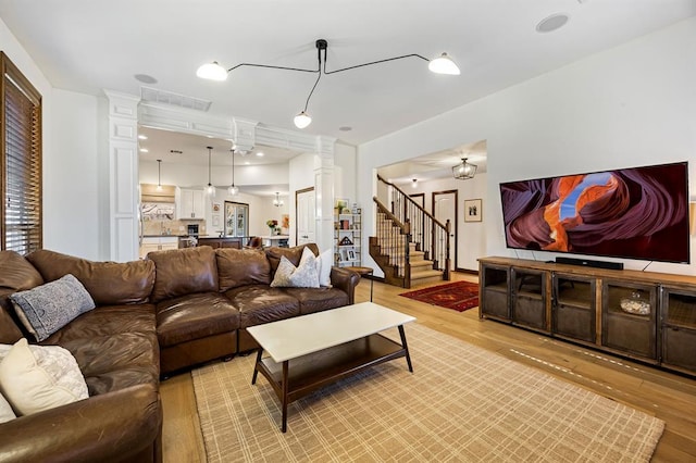 living room with decorative columns, visible vents, light wood-style flooring, and stairs