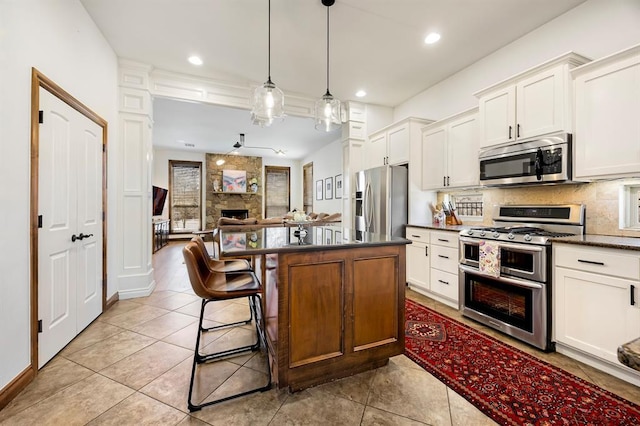 kitchen featuring a stone fireplace, dark countertops, tasteful backsplash, and appliances with stainless steel finishes