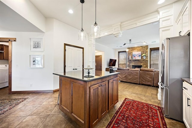 kitchen with dark countertops, freestanding refrigerator, a barn door, a stone fireplace, and washer / dryer