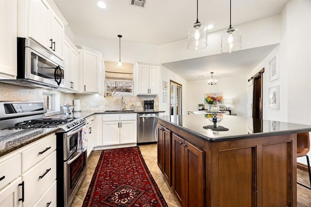 kitchen with a sink, stainless steel appliances, white cabinetry, a barn door, and tasteful backsplash