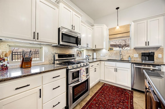 kitchen with decorative backsplash, dark stone countertops, appliances with stainless steel finishes, white cabinets, and a sink