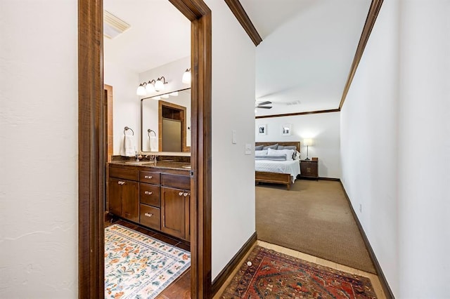 hall featuring carpet flooring, crown molding, baseboards, and a sink