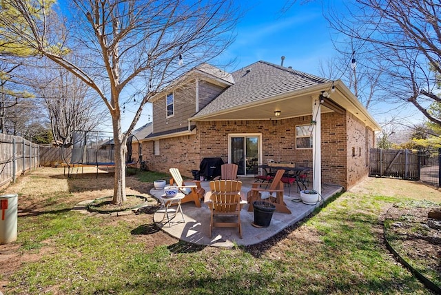 rear view of house featuring brick siding, a fenced backyard, a patio, and a trampoline