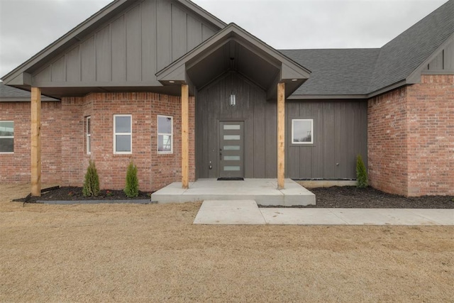 entrance to property featuring brick siding, board and batten siding, and roof with shingles