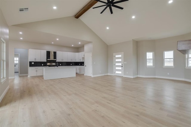 unfurnished living room with baseboards, visible vents, beamed ceiling, light wood-type flooring, and high vaulted ceiling